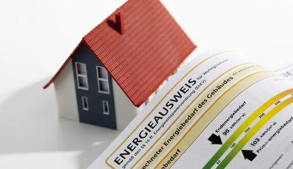 Hausbesitzer hält einen Energieausweis vor einem Einfamilienhaus in der Hand